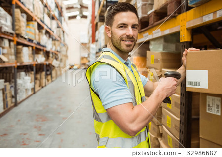 Male warehouse worker in safety vest scanning box on shelf with scanner in aisle, copy space 132986687