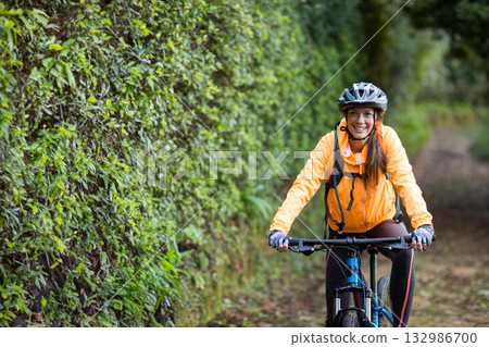 Female cyclist sporting helmet and backpack riding mountain bike along leafy dirt trail, copy space Female cyclist sporting helmet and backpack riding mountain bike along leafy dirt trail, copy space 132986700