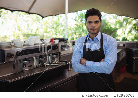 Middle Eastern male barista pouring milk into cups on espresso machine under umbrella, copy space Middle Eastern male barista pouring milk into cups on espresso machine under umbrella, copy space 132986705