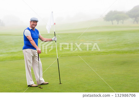 Senior African American man standing on putting green gripping flagstick and golf club, copy space Senior African American man standing on putting green gripping flagstick and golf club, copy space 132986706