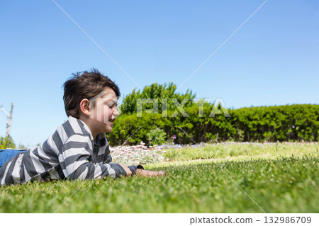 School-age boy lying on grassy lawn checking smartwatch among small flowers outdoors, copy space School-age boy lying on grassy lawn checking smartwatch among small flowers outdoors, copy space 132986709