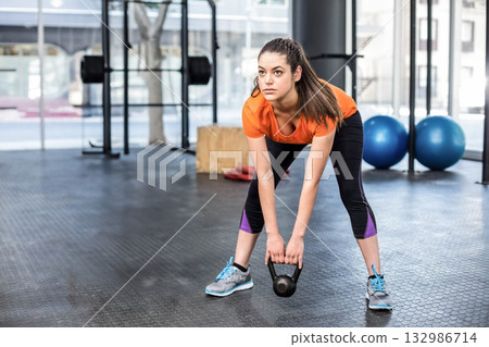 Woman in orange sports shirt lifting kettlebell in gym with weight racks and blue stability balls Woman in orange sports shirt lifting kettlebell in gym with weight racks and blue stability balls 132986714