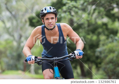 Male cyclist riding mountain bike along dirt trail in park wearing helmet and fingerless gloves Male cyclist riding mountain bike along dirt trail in park wearing helmet and fingerless gloves 132986761