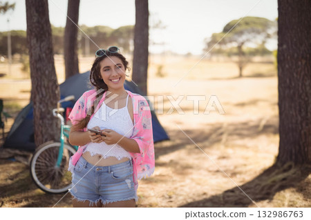 Teenage girl texting on smartphone at forest camp near tent and bicycle wearing sunglasses Teenage girl texting on smartphone at forest camp near tent and bicycle wearing sunglasses 132986763