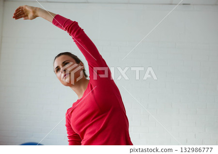 Woman stretching sideways against white brick wall in studio with blue exercise ball, copy space Woman stretching sideways against white brick wall in studio with blue exercise ball, copy space 132986777