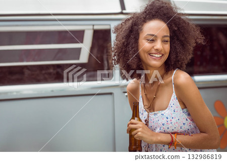 African American woman leaning on blue camper van outside holding brown glass bottle, copy space African American woman leaning on blue camper van outside holding brown glass bottle, copy space 132986819