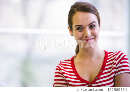 Female wearing red and white striped top smiling gently while standing by bright window, copy space Female wearing red and white striped top smiling gently while standing by bright window, copy space 132986834