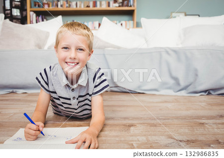 School-age boy wearing striped polo drawing with blue marker on paper in living room 132986835