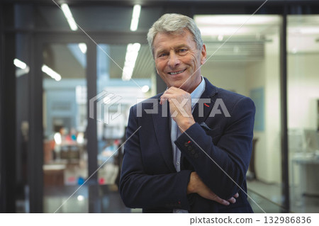 Senior man wearing business attire standing in modern office among glass partitions, LED lights Senior man wearing business attire standing in modern office among glass partitions, LED lights 132986836