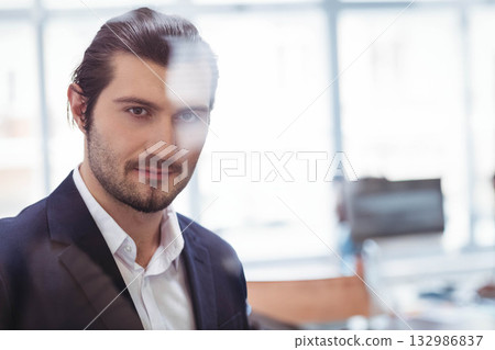 Man standing behind glass partition at modern office desk, viewing computer monitor, copy space 132986837