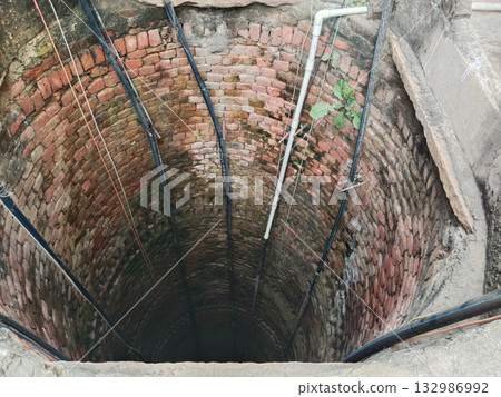 Brick-lined traditional well interior with multiple plastic pipes installed for submersible pump system in rural Indian irrigation setup Brick-lined traditional well interior with multiple plastic pipes installed for submersible pump system in rural Indian irrigation setup 132986992