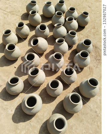 Multiple raw clay matkas arranged outdoors under direct sunlight for drying, top view of traditional earthen pots in rural pottery scene Multiple raw clay matkas arranged outdoors under direct sunlight for drying, top view of traditional earthen pots in rural pottery scene 132987027
