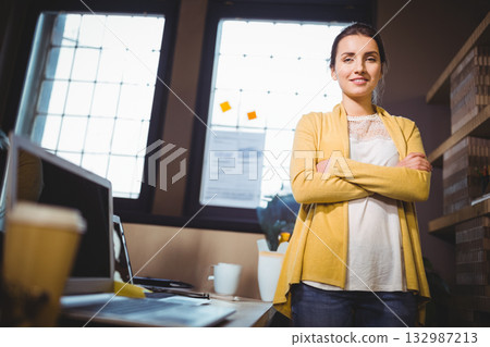 Woman standing in creative office organizing papers on desk near laptop and coffee cup, copy space 132987213
