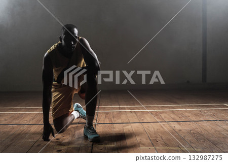 African American man wearing yellow jersey kneeling on basketball court boundary lines holding ball 132987275