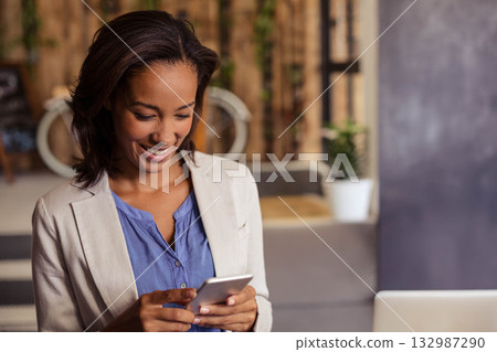 African American woman wearing blazer at coworking space checking smartphone by laptop, copy space African American woman wearing blazer at coworking space checking smartphone by laptop, copy space 132987290