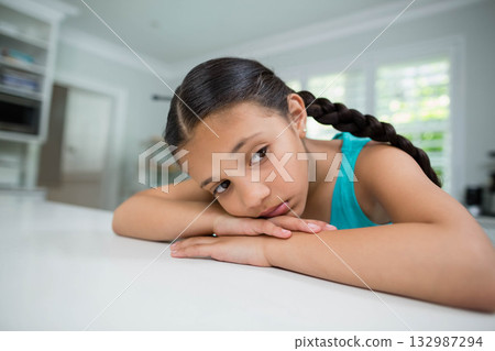 Girl leaning on white countertop by shuttered window in kitchen wearing turquoise top gazing out 132987294