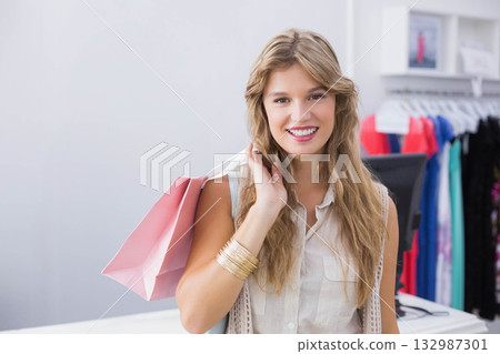 Female shopper carrying pastel pink bags on arm in clothing store near racks, checkout screen Female shopper carrying pastel pink bags on arm in clothing store near racks, checkout screen 132987301