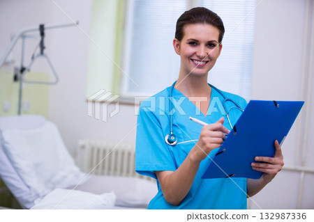 Female nurse holding clipboard and stethoscope in scrubs by bed trapeze lift in clinic, copy space 132987336