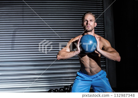 Shirtless athletic man holding medicine ball and squatting beside kettlebells at gym, copy space Shirtless athletic man holding medicine ball and squatting beside kettlebells at gym, copy space 132987348