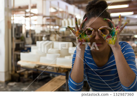 Female artist standing in pottery studio covering hands with paint near ceramic bowls, copy space 132987360