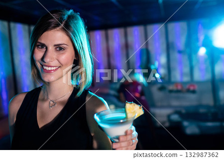 Female patron smiling and holding martini glass with pineapple at bar by wall panels 132987362