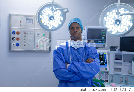 Mid adult male surgeon wearing blue surgical gown in operating room under lights, watching monitor 132987367