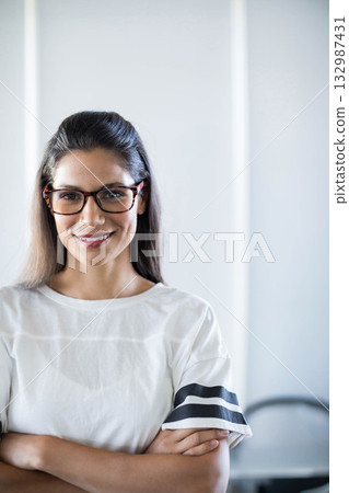 Woman wearing rectangular glasses standing in office against wall with light strips, blurred chair Woman wearing rectangular glasses standing in office against wall with light strips, blurred chair 132987431