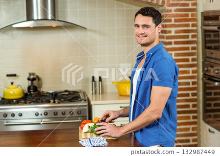 Man chopping green bell pepper on wooden countertop in home kitchen with knife, copy space Man chopping green bell pepper on wooden countertop in home kitchen with knife, copy space 132987449