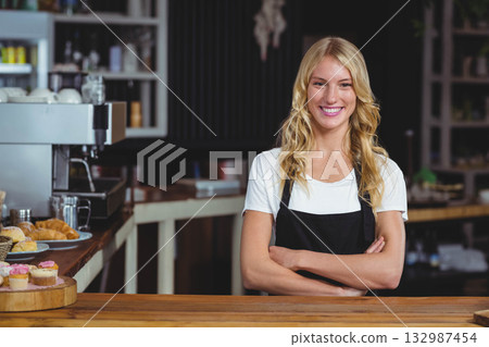 Smiling female barista wearing apron behind counter at cafe with espresso machine, copy space 132987454