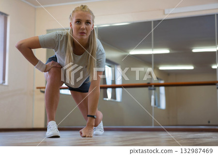 Female athlete performing low lunge on studio floor wearing fitness tracker and wrist support Female athlete performing low lunge on studio floor wearing fitness tracker and wrist support 132987469