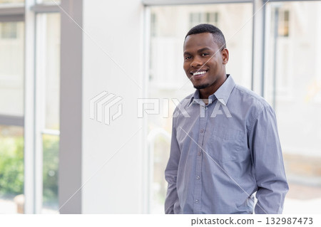 African American man standing in office lobby by large glass windows with green foliage, copy space African American man standing in office lobby by large glass windows with green foliage, copy space 132987473