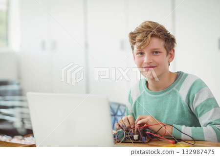 Male child assembling circuit with wires on wooden table in home study beside laptop, copy space 132987475