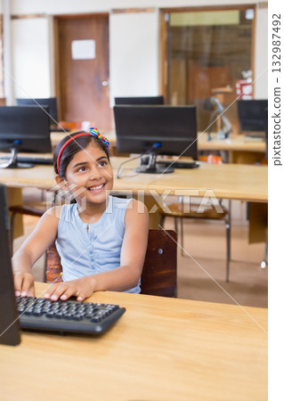 Indian girl child typing on keyboard at school computer lab with desktop monitor and wooden desk Indian girl child typing on keyboard at school computer lab with desktop monitor and wooden desk 132987492