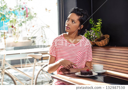 African American woman pointing at chocolate cake with cherry near coffee cup looking right in cafe African American woman pointing at chocolate cake with cherry near coffee cup looking right in cafe 132987530
