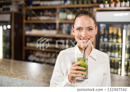 Female bartender standing behind bar counter serving cocktail with lime slices mint ice black straw 132987592