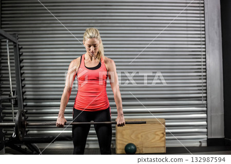 Mid-adult woman in sportswear holding loaded barbell at thigh level in gym amid squat rack Mid-adult woman in sportswear holding loaded barbell at thigh level in gym amid squat rack 132987594