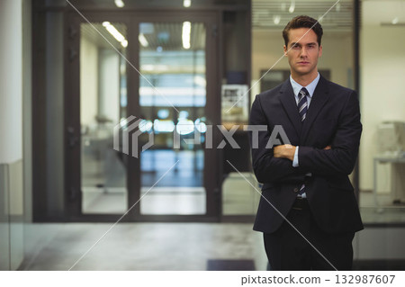 Male in business attire standing arms crossed in lobby near glass doors and printer, copy space Male in business attire standing arms crossed in lobby near glass doors and printer, copy space 132987607