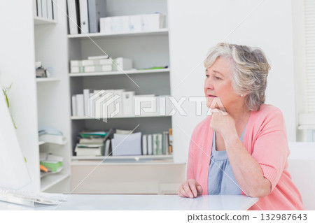 Senior woman leaning on hand and gazing at computer monitor at desk with plant, copy space 132987643