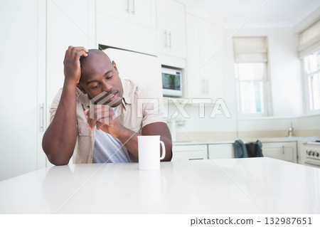 African American man leaning forward and holding ceramic coffee mug on countertop in home kitchen African American man leaning forward and holding ceramic coffee mug on countertop in home kitchen 132987651