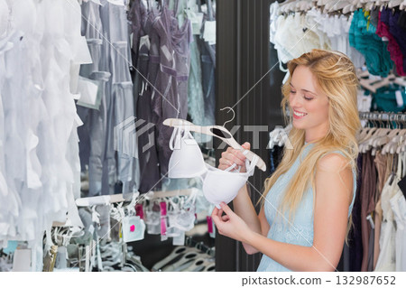 Woman shopper holding white bra on hanger examining lingerie racks at shop in dress, copy space 132987652
