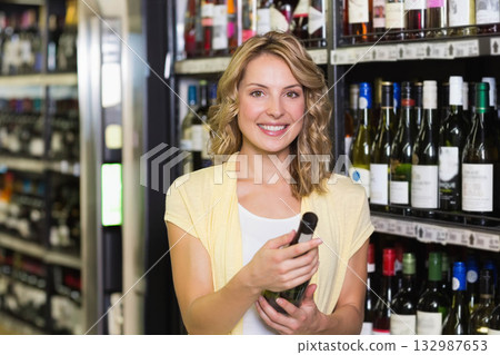 Woman holding green wine bottle and smiling in liquor store aisle with metal shelving Woman holding green wine bottle and smiling in liquor store aisle with metal shelving 132987653