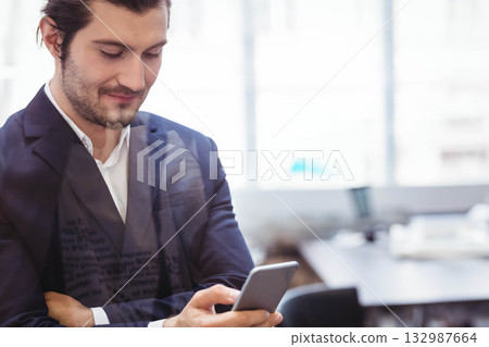 Man in navy blazer holding smartphone and checking messages at office desk with laptop, copy space 132987664