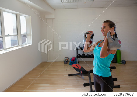 Female fitness enthusiast in athletic attire lifting kettlebell in home gym with bench copy space Female fitness enthusiast in athletic attire lifting kettlebell in home gym with bench copy space 132987668