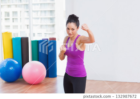 Asian woman practicing boxing stance on floor in fitness studio with foam rollers, exercise balls Asian woman practicing boxing stance on floor in fitness studio with foam rollers, exercise balls 132987672