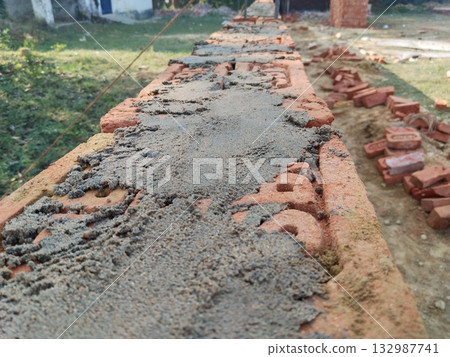 Closeup view of bricklaying process with cement mortar applied on red bricks for boundary wall construction in rural area, traditional masonry technique in Indian village construction work Closeup view of bricklaying process with cement mortar applied on red bricks for boundary wall construction in rural area, traditional masonry technique in Indian village construction work 132987741