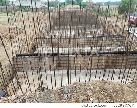 Building construction site with steel reinforcement bars, concrete formwork, and foundation framework in progress for modern multi-story structure development 132987767
