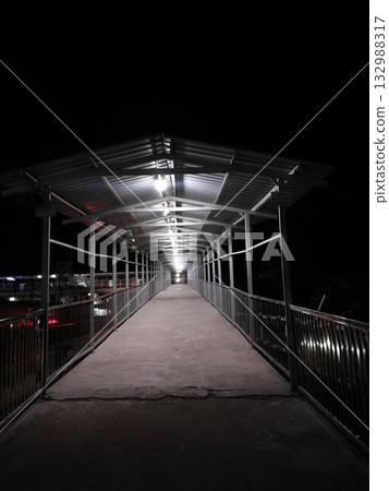 Railway station foot overbridge at night with roof and lights empty pedestrian walkway over train tracks Railway station foot overbridge at night with roof and lights empty pedestrian walkway over train tracks 132988317