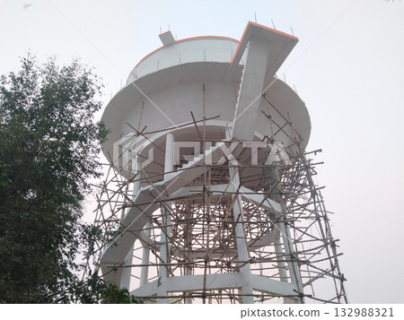 Overhead water tank under construction with bamboo scaffolding and spiral staircase in rural India, infrastructure development and public water supply system in progress 132988321