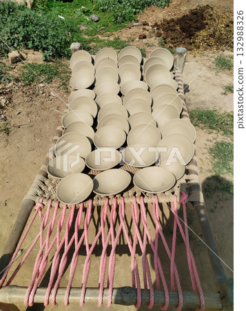Earthen parai dish made of raw clay placed on traditional cot under sunlight for drying in rural Indian setting 132988326