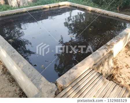Small four-cornered brick boundary structure used to store or hold water temporarily in rural area, showing simple low wall construction for water containment in agricultural field 132988329